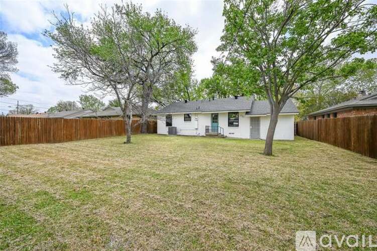 A backyard with a white house, two trees, and a fence.