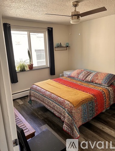 A bedroom with a bed covered in a multicolored blanket.