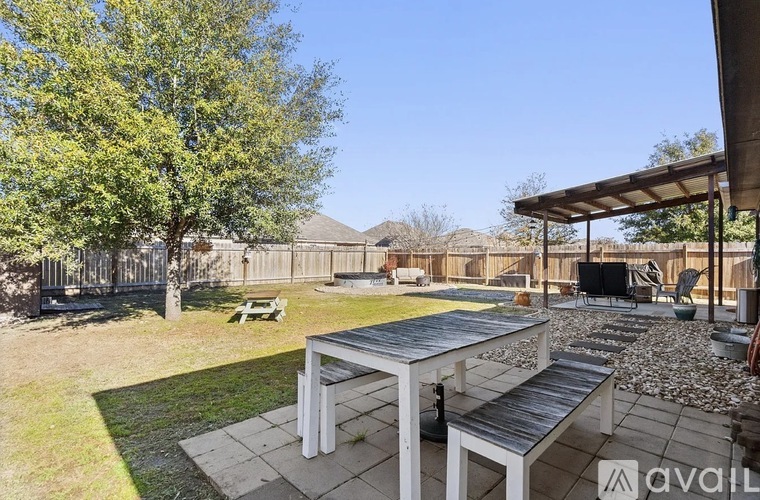 A patio with a table and chairs is surrounded by a grassy area and trees.