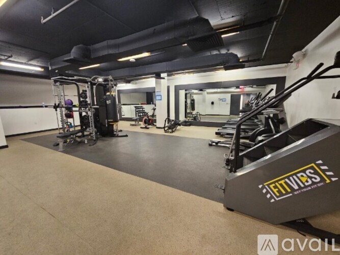A gym with a variety of equipment including a squat rack, a bench press, and a weight machine.