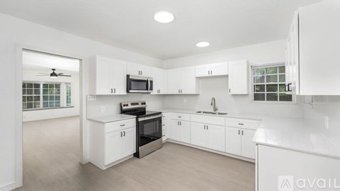 A kitchen with white cabinets and appliances, a window with a fan, and a sink with a faucet.