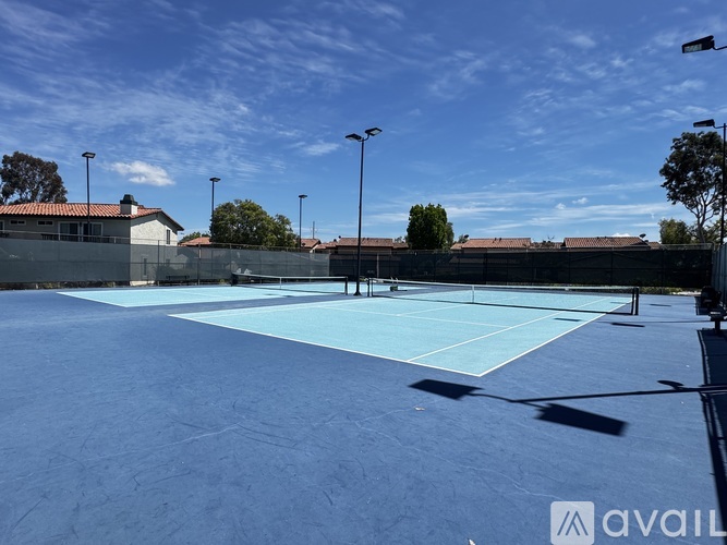 A tennis court with a blue surface and white lines, surrounded by a fence and trees.