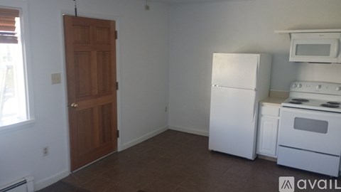 A kitchen with white appliances and a wooden door.