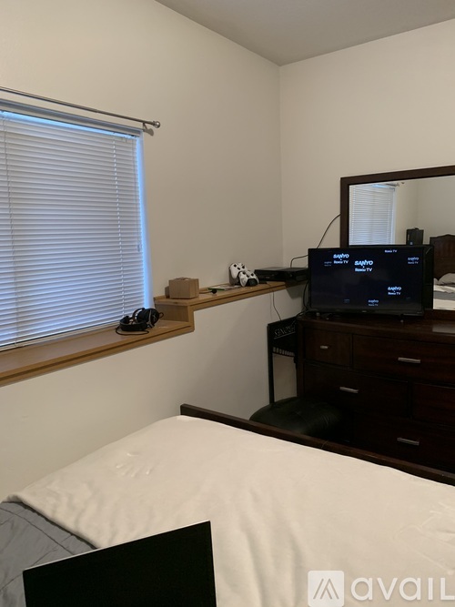 A bedroom with a bed, a TV, a mirror, and a window with blinds.