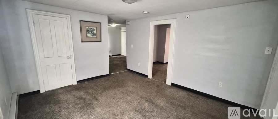 A spacious room with a door on the left and a hallway leading to another room on the right.
