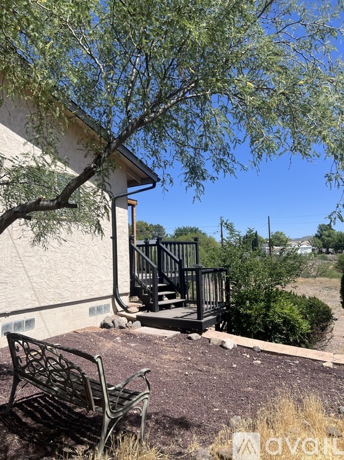 A bench is in front of a building with a tree and a railing.