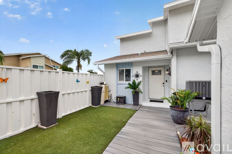 A white house with a wooden deck and a green lawn.