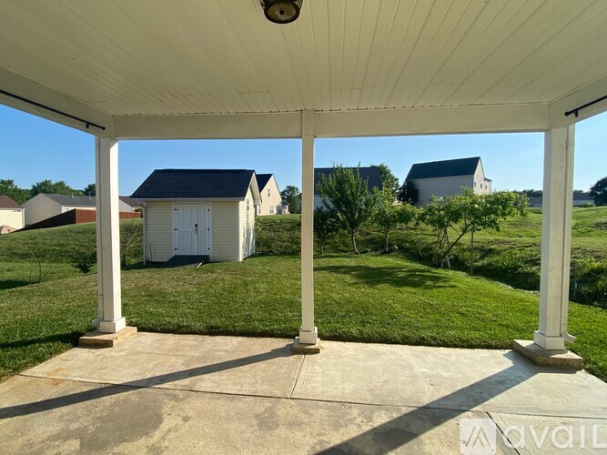 A white porch with a view of a white house and green grass.