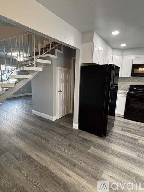 A black refrigerator in a kitchen with a staircase in the background.