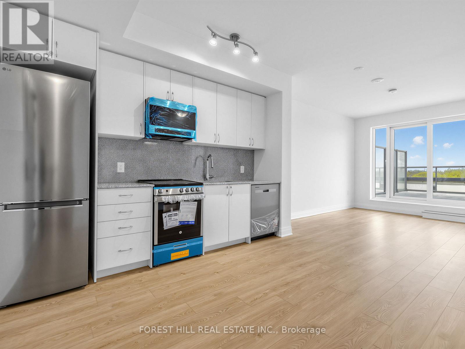 A modern kitchen with a stainless steel refrigerator and wooden flooring.