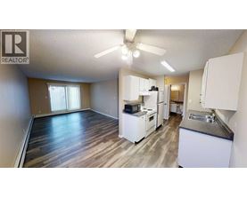 A well-lit, spacious kitchen and living area with wood flooring and white appliances.