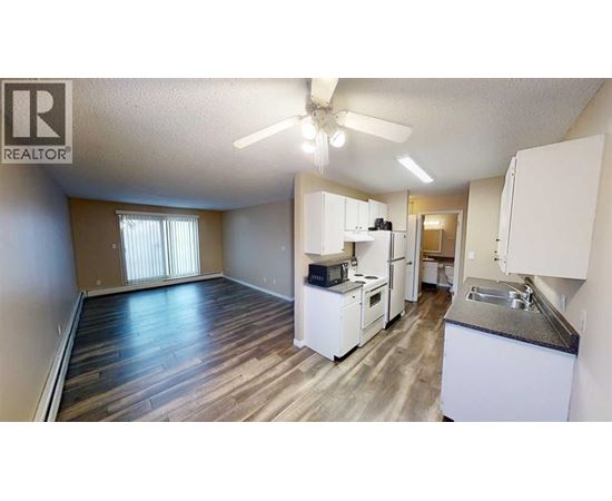 A well-lit, spacious kitchen and living area with wood flooring and white appliances.