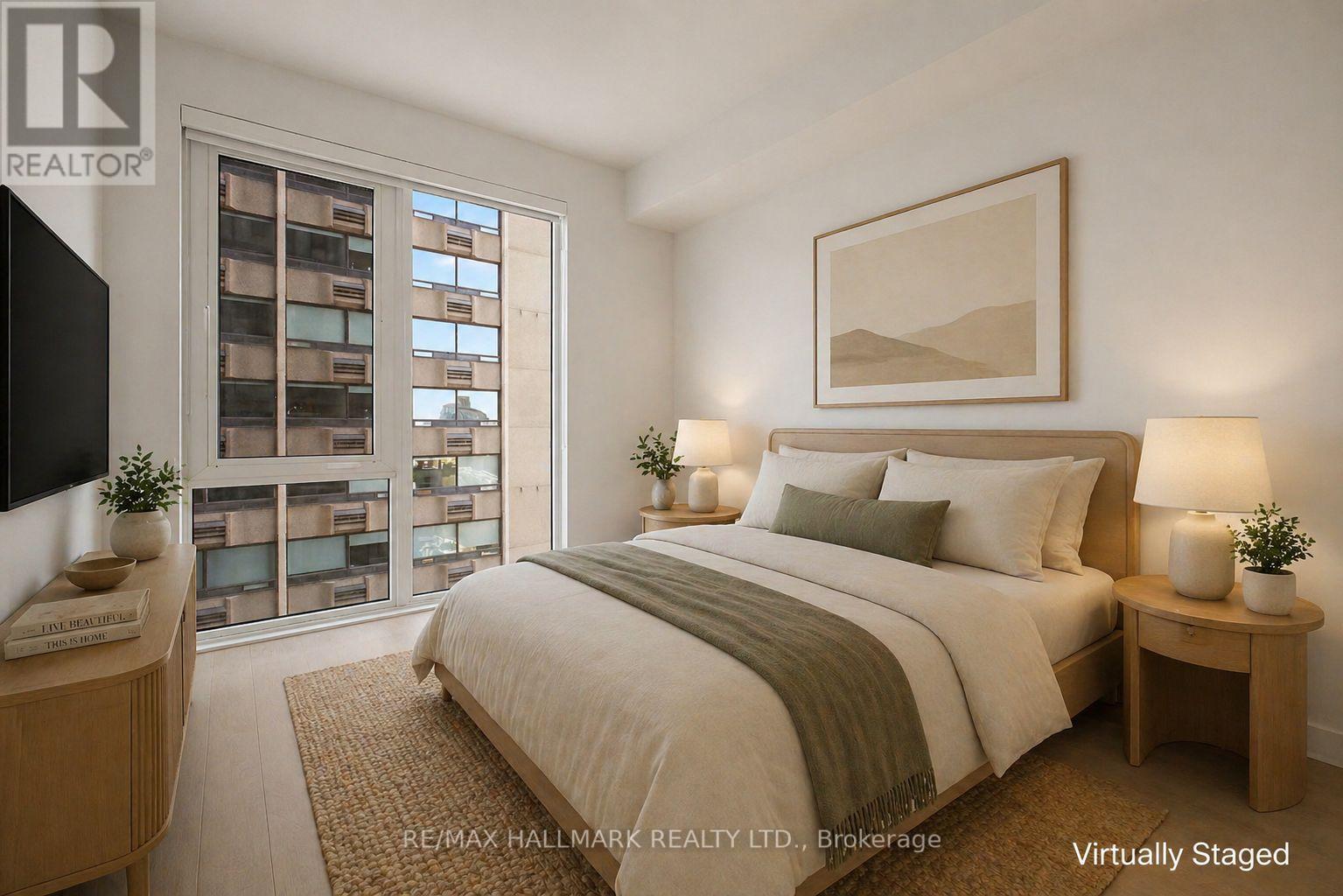 A bedroom with a large bed, a nightstand, and a window with a view of a building.
