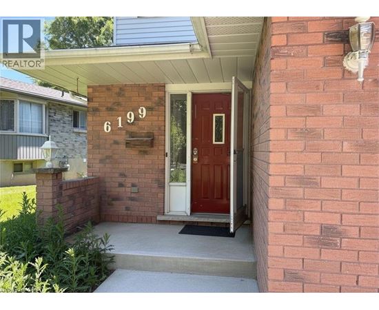 A red door with the number 6199 on the brick wall above it.