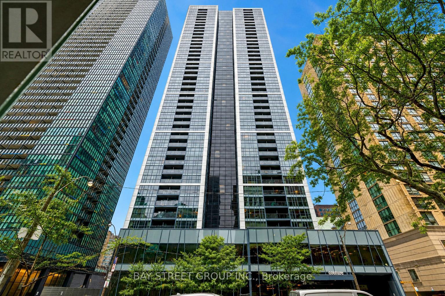 A tall building with a glass facade stands in front of a tree.