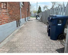 A blue trash bin sits on a brick pathway next to a wooden fence.