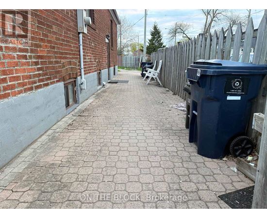 A blue trash bin sits on a brick pathway next to a wooden fence.