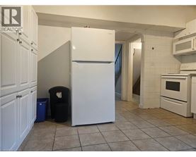 A white refrigerator in a kitchen with a black trash can and blue trash bag.