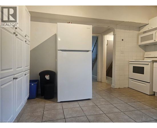 A white refrigerator in a kitchen with a black trash can and blue trash bag.