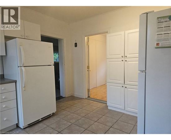 A white refrigerator is in a kitchen with a white door and a white cabinet.