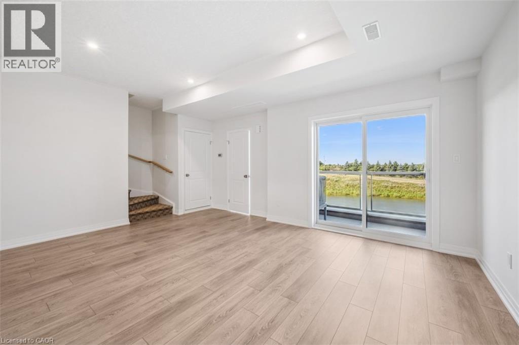 A spacious room with wooden flooring and a large window overlooking a grassy area.