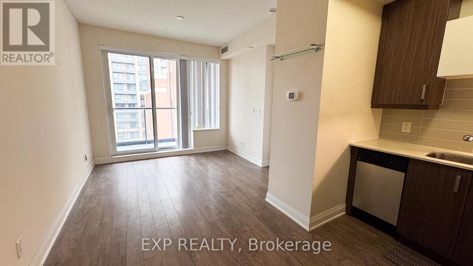 A realtor photo of an empty apartment with wood floors and a kitchen area.