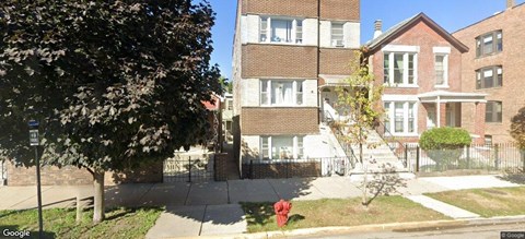 A tree is in front of a building with a red fire hydrant in front of it.