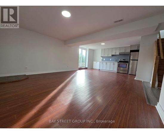 A spacious room with wooden flooring and a kitchen area in the background.