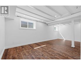 A room with wooden flooring and white walls, with a window and a door frame visible.
