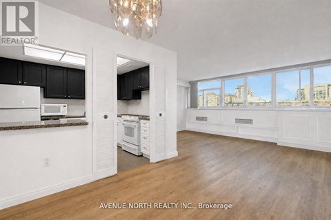 A large, empty room with a kitchen area and a chandelier.