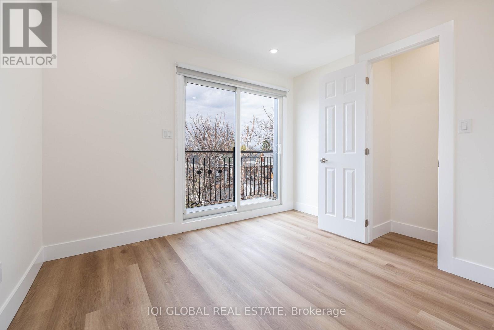 A room with a white door and a window with a view of a fence and trees.