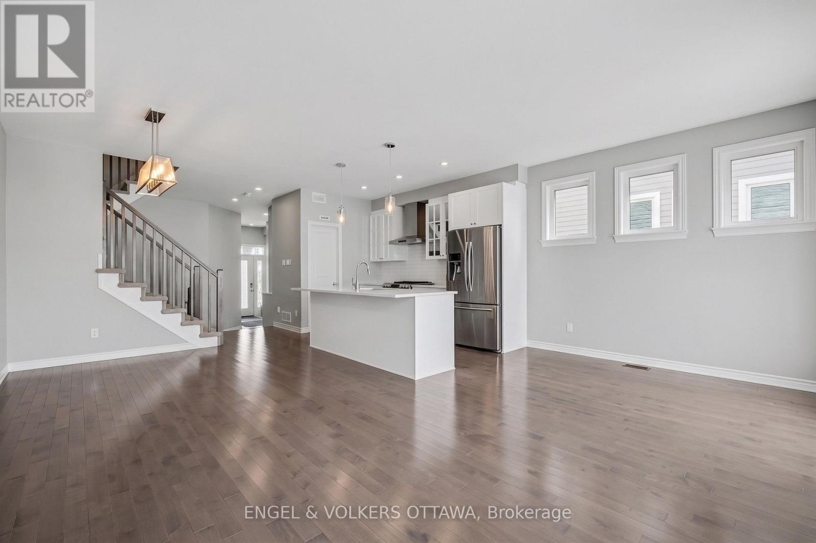 A spacious, empty room with wood flooring and a staircase leading to the upper level.