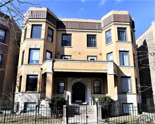 A large, two-story building with a black metal fence in front.