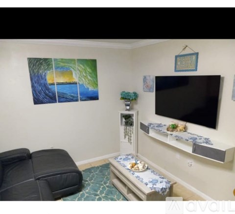 A living room with a black leather couch, a television, and a painting of a wave on the wall.