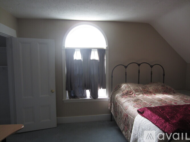 A bedroom with a bed, a window with curtains, and a door.