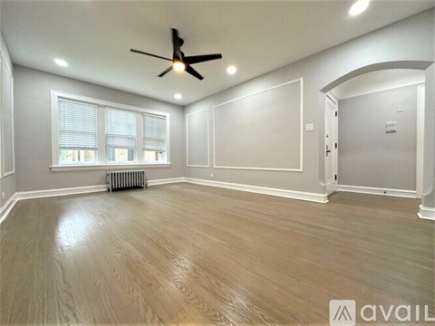 A spacious room with a ceiling fan and lighting, featuring a wooden floor and white walls.
