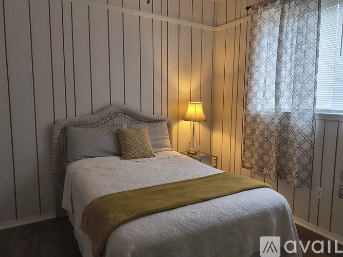 A bedroom with a bed, pillows, a lamp, and a window with curtains.