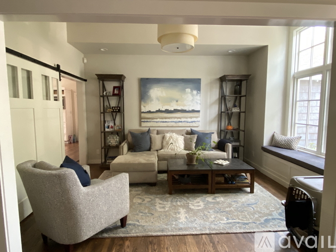 A living room with a grey armchair, a white sofa, a wooden coffee table, and a painting on the wall.