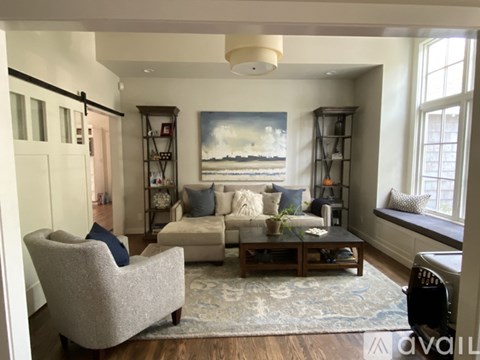 A living room with a grey armchair, a white sofa, a wooden coffee table, and a painting on the wall.