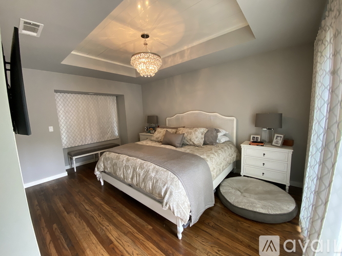 A bedroom with a large bed, a chandelier, and a TV mounted on the wall.