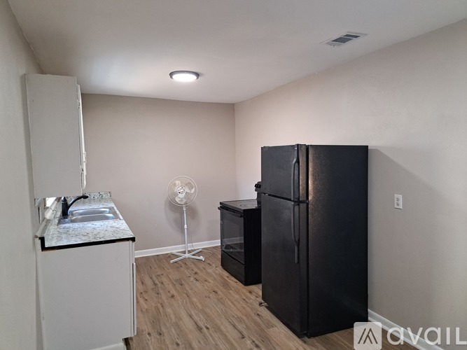 A kitchen with a black fridge, a white sink, and a white cabinet.