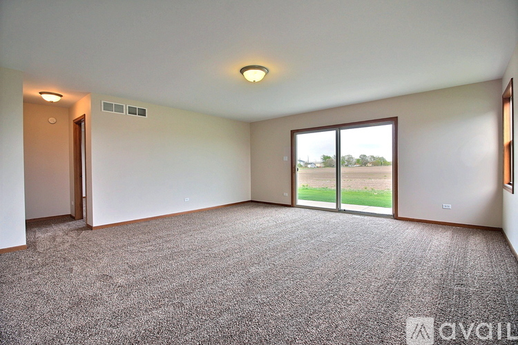 A spacious room with a carpeted floor and sliding glass doors leading to a green outdoor area.