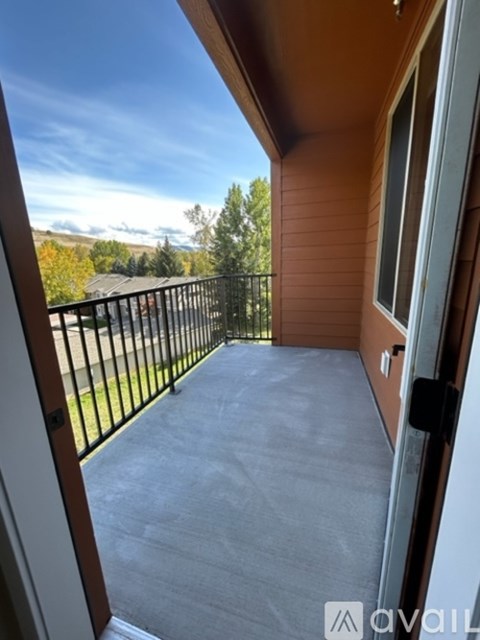 A balcony with a black railing and a view of trees and houses in the distance.