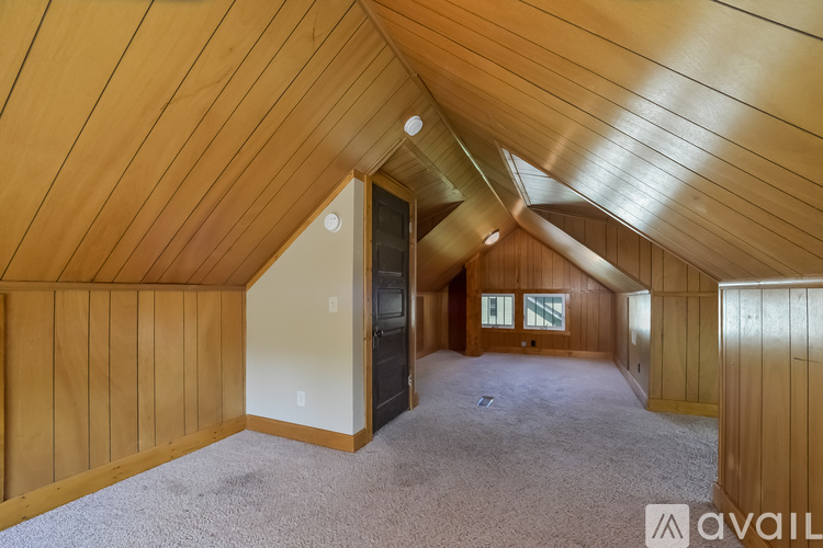 A spacious attic room with wooden walls and a carpeted floor.