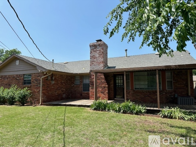 A house with a brick exterior and a chimney is surrounded by greenery.