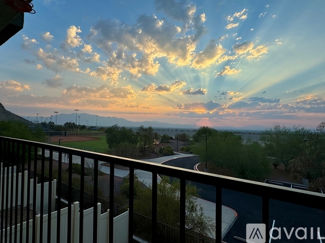 A sunset view from a balcony with a road and greenery in the distance.