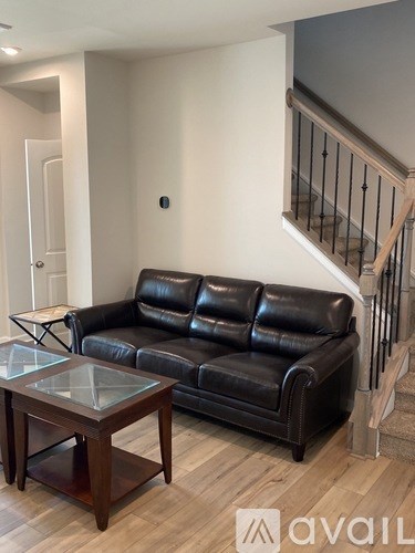 A black leather couch sits in a living room with a glass coffee table in front of it.