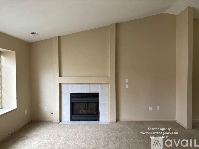 A large empty room with a fireplace and carpeted floor.