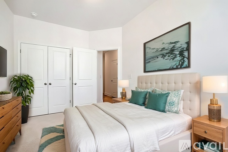 A bedroom with a large bed, a painting on the wall, and a lamp on the side table.