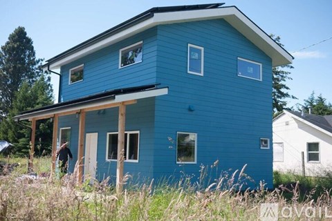 A blue house with a white roof and a person standing in front of it.